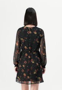 Robe noire à fleurs avec des manches transparentes à pois, une taille élastique et une jupe fluide. Comprend des motifs floraux colorés et une fermeture dans le dos.