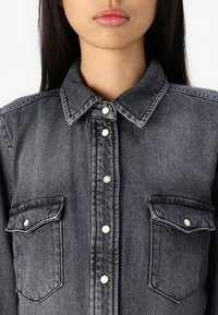 Mørkeblå denimskjorte med krage, perlemorsnapper og to brystlommer. Strukturert stoff med en litt falmet overflate.