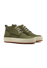 Chaussures chukka en suede vert avec des semelles en caoutchouc blanches et des accents marron. Les caractéristiques incluent des œillets en métal et un dessus texturé.