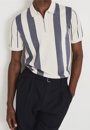 Polo a righe in maglia con maniche corte, caratterizzato da una mezza zip, in colori crema e navy, con tessuto texture, abbinato a pantaloni scuri.