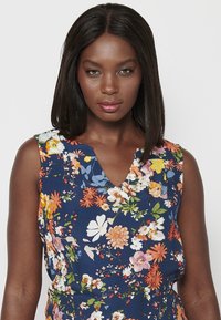 Bloemen sleeveless jurk met een marineblauwe achtergrond. Kenmerkt zich door levendige, kleurrijke bloemen, een V-halslijn en een zachte textuur.
