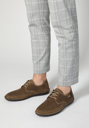 Braune durchbrochene Leder Schuhe mit beigen Schnürsenkeln und einer schwarzen Gummisohle, getragen mit hellgrauen Karohosen.
