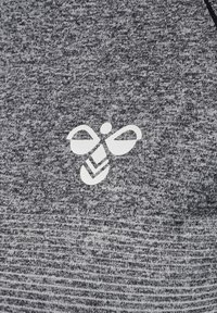 Logo d'abeille blanc stylisé sur tissu gris texturé, probablement une partie d'un vêtement.