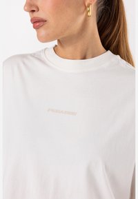 White cotton t-shirt featuring a crew neckline and a subtle embossed logo "PEGADOR" in light pink on the front. Smooth texture.