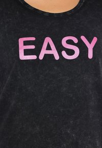 Černé tričko s mírně texturovanou tkaninou. Tučně lesklá růžová písmena tvoří slovo "EASY" na přední straně. Kulatý výstřih.