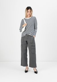 Gestreiftes langärmliges Oberteil in Marineblau und Weiß; graue Cargo-Hose mit Seitentaschen; schwarze spitze Ballerinas; einfache Umhängetasche.