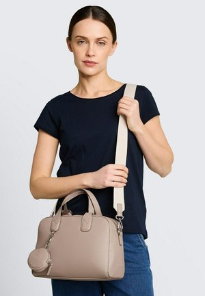 Femme portant un haut noir et un jean bleu, portant un sac à main en cuir beige avec une bandoulière large amovible et une petite pochette ronde pour pièces.