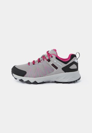 Zapato de senderismo ligero con parte superior de malla gris y acentos en rosa, además de una puntera de goma negra, diseñado para ofrecer tracción y comodidad.
