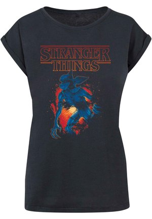 Czarny bawełniany t-shirt z grafiką niebieskiego stwora z czerwonymi i pomarańczowymi akcentami, oznaczony napisem "Stranger Things" w odważnym pomarańczowym kolorze.
