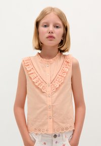Pfirsichfarbenes ärmelloses Top mit Rüschenspitze, besticktem Blumenmuster und Knopfverschluss. Der gewellte Saum sorgt für Textur.