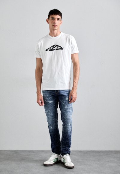 White short-sleeve t-shirt with black graphic print, paired with light blue distressed skinny jeans and white sneakers with green stripes.