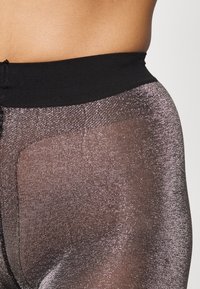 Leggings neri trasparenti con finitura metallica, caratterizzati da una ampia fascia in vita nera e una finitura texturizzata, che mette in risalto un sottile effetto luccicante.