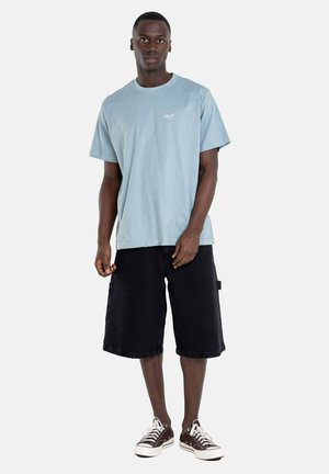Light blue cotton t-shirt with a crew neck, paired with black knee-length shorts and brown sneakers. Simple design without patterns.