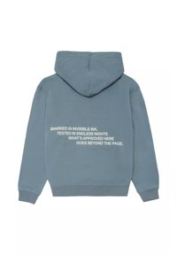 Sudadera con capucha en azul apagado, con texto blanco en la parte trasera: "MARCA EN TINTA INVISIBLE, PROBADO EN NOCHES INFINITAS..." El texto es en negrita y está centrado.