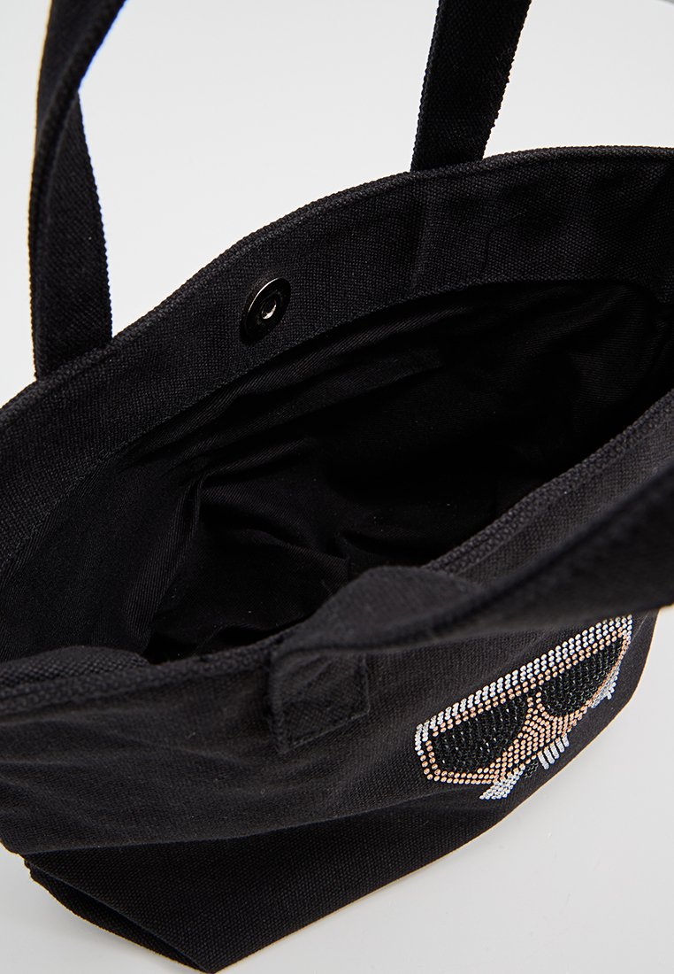 Sac fourre-tout noir en toile, avec une doublure intérieure, deux poignées et un motif de crâne en strass. Comprend une fermeture à pression.