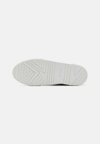 Semelle de sneaker blanche avec une surface texturée, ornée de motifs en zigzag et de marquages. Matériau en caoutchouc, avec une forme plate et des bords réguliers.