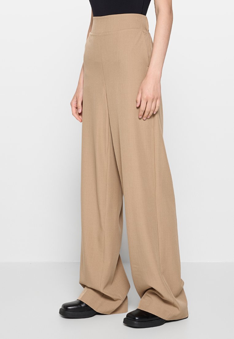 Beige wijde broek met hoge taille, gemaakt van lichtgewicht stof. Heeft een gladde textuur en een minimalistisch ontwerp.