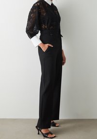 Czarna koronkowa bluzka z długimi, obszernej rękawami oraz białą koszulą z kołnierzykiem pod spodem. Czarne spodnie z wysokim stanem, z bocznymi kieszeniami.