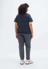 Μπλε ριγωτό κοντομάνικο τοπ με άνετη εφαρμογή, σε συνδυασμό με γκρι παντελόνια και λευκά αθλητικά παπούτσια. Σγουρά μαλλιά, από πίσω.