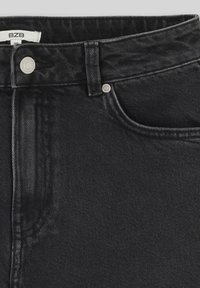 Jean en denim noir avec une fermeture à bouton à l'avant, un bouton métallique unique en accent, et un detail de poche avant avec une finition légèrement texturée.