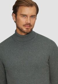 Szary sweter typu golf wykonanego z cienkiej dzianiny, charakteryzujący się dopasowanym krojem oraz prążkowanym kołnierzem, co dodaje tekstury i detalu.