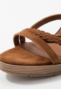 Brown suede sandal with braided strap design, flat platform sole, rounded toe, and textured footbed for comfort.