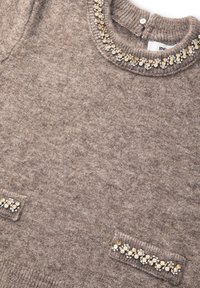 Brązowy dzianinowy top bez rękawów z okrągłym dekoltem i dwiema kieszeniami, ozdobiony złotymi i przezroczystymi kamieniami dekoracyjnymi.