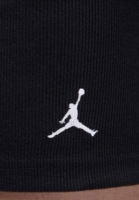 Svart ribbad tygshorts med en vit broderad Jumpman-logotyp nära fållen. Texturerad yta med en åtsittande design.