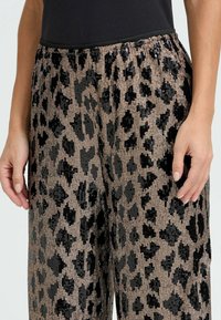 Sorte og gyldne leopardprintbukser med en paliettekstur; elastisk talje; bred ben silhuet; blødt, let stof.