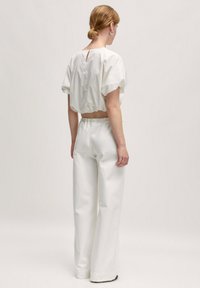 Witte cropped top met pofmouwen en een keyhole-detail aan de achterkant, gecombineerd met witte high-waisted broek met wijde pijpen, van een gladde stof.