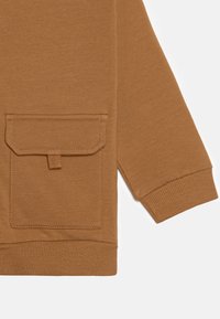 Tejido de sudadera marrón con un bolsillo parche frontal, puños acanalados y una textura suave. El diseño presenta un ajuste relajado y una construcción simple.