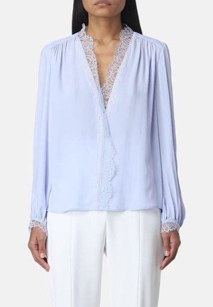 Blusa di un azzurro chiaro con scollo a V, rifinita con pizzo lungo il colletto e i polsini, e maniche lunghe. Il tessuto è liscio con una leggera lucentezza.