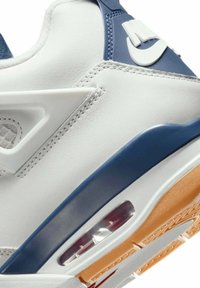 Zapatilla blanca con un upper de cuero suave y acentos en navy, una unidad de amortiguación de aire visible y una suela texturizada con un patrón de goma.