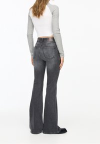 Vaqueros acampanados grises con un acabado desgastado, cinco bolsillos y una etiqueta de cuero en la cintura trasera. Estilizados con una blusa de punto de manga larga.