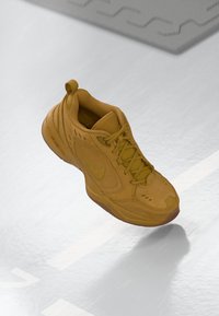 Bruine Nike-sneaker die in de lucht hangt met zichtbare Air-zool en veters, tegen een reflecterende ondergrond met witte lijnen.