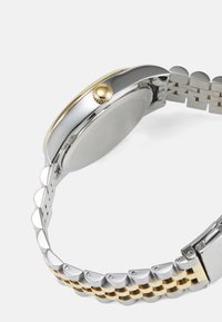 Silver and gold-tone metal wristwatch with a round case, smooth bezel, and a patterned band featuring alternating silver and gold links.