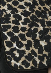 Dekorativna tkanina sa bež pozadinom i crno-bijelim leopard uzorkom. Ivica je završena crnim obrubom. Ima teksturirani izgled.