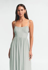 Šviesiai žalia maksima su plonomis petnešomis, tekstūruotu audiniu, prigludusia liemene ir plačiu sijonu. Paprastas, elegantiškas dizainas.