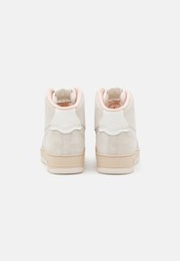 High-top sneakers in light beige suede with white leather accents and a pale pink inner lining. Features a textured back panel.