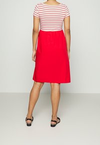 Kortärmad klänning med en randig vit och röd topp och en klar röd kjol. Klänningen har en avslappnad passform som når mitt på vaden.