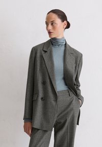 Grijze pinstripe blazer met een dubbelreeks ontwerp, zwarte knopen en notch revers, gecombineerd met een lichtblauwe coltrui.