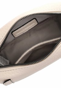 Interno della borsa color crema con texture liscia, dotato di chiusura con zip, rivestimento in tessuto e un'etichetta cucita all'interno.