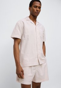 Σετ πυτζάμας με κοντά μανίκια και κουμπιά σε απαλό ροζ με λευκές ρίγες. Διαθέτει τσέπη στο στήθος, άνετη εφαρμογή και ταιριαστά σορτς.