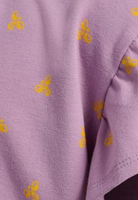 Fioletowy bawełniany t-shirt z powtarzającym się wzorem żółtych pszczół. Materiał ma miękką fakturę i lekko elastyczny krój przy rękawach.