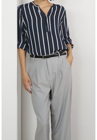 Blouse rayée bleu marine et blanche avec un col en V, manches retroussées, assortie à un pantalon taille haute gris clair et une ceinture noire.