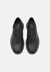 Scarpe in pelle nera con finitura liscia, dotate di chiusura con zip sulla parte superiore, punta arrotondata e suola bassa in gomma. Branding rosso all'interno.