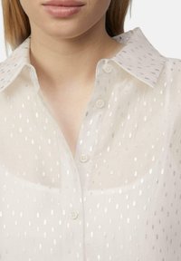 Sheer white blouse with silver dot pattern, classic collar, and button-up front. Soft fabric with a lightweight texture.