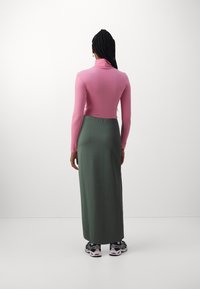 Langarmige roze top met een hoge hals, gecombineerd met een groene maxi rok. Gemaakt met zwarte sneakers met witte en rode accenten.
