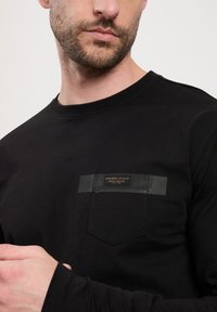 Czarny longsleeve t-shirt z okrągłym dekoltem wykonany z bawełny. Charakteryzuje się kieszonką na piersi z ciemną metką oraz gładką fakturą.