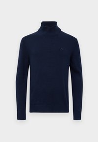 Pulover turtleneck raiat de culoare bleu marin, cu mâneci lungi și un mic logo roșu, alb și albastru pe pieptul stâng.